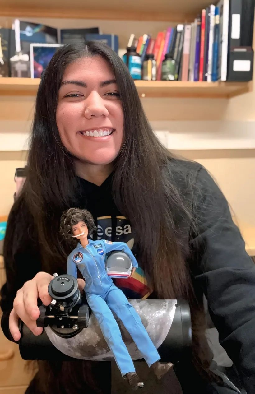 Carol Jiménez sonriendo en su escritorio, con una muñeca astronauta en las manos