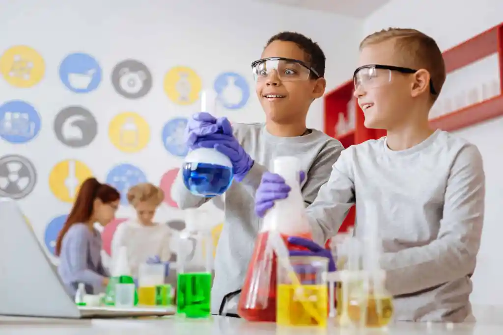 Dos niños con gafas y guantes de laboratorio manipulando un líquido azul